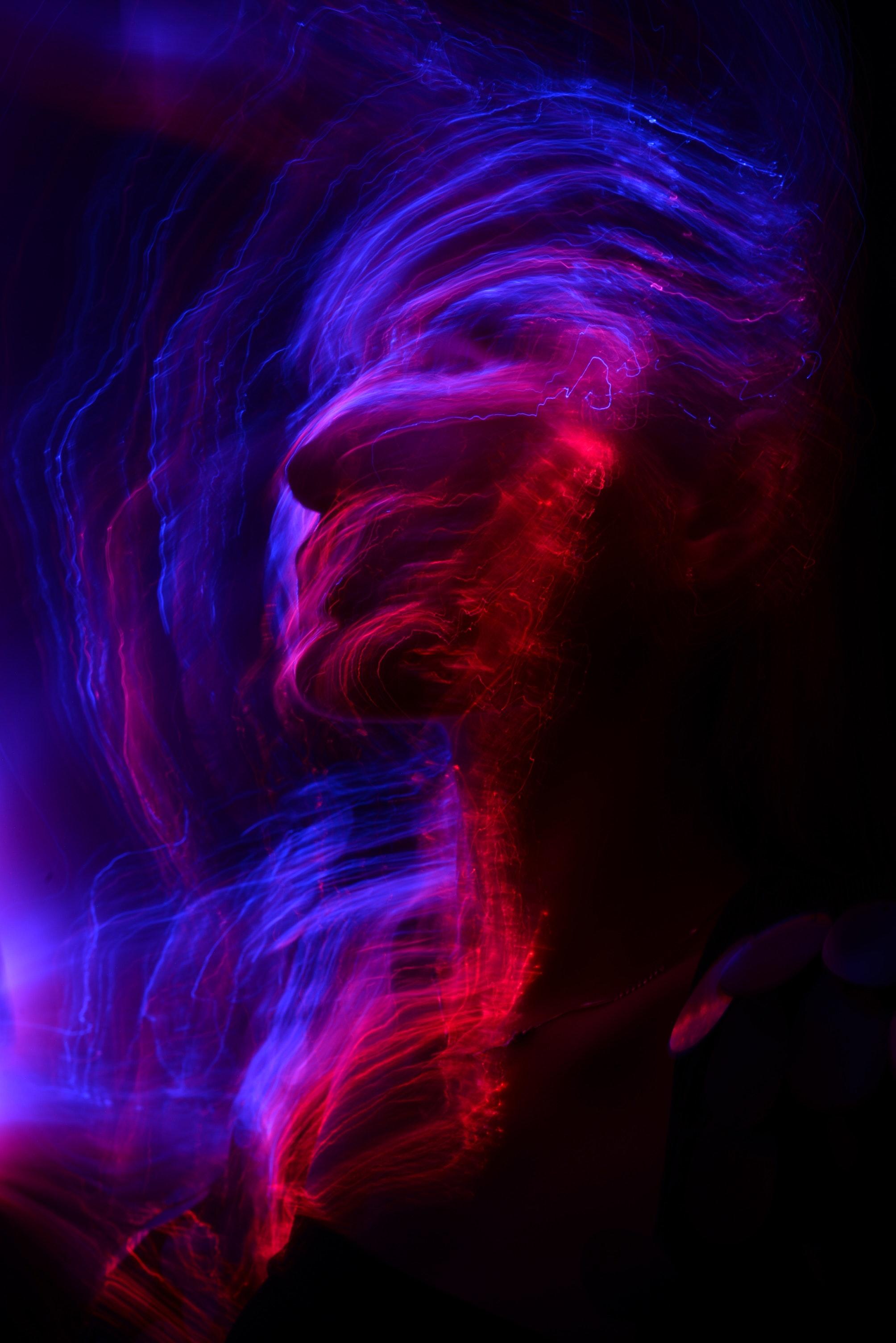 Simulación de rostro humano con trazos de luz en azul, rosa y rojo.